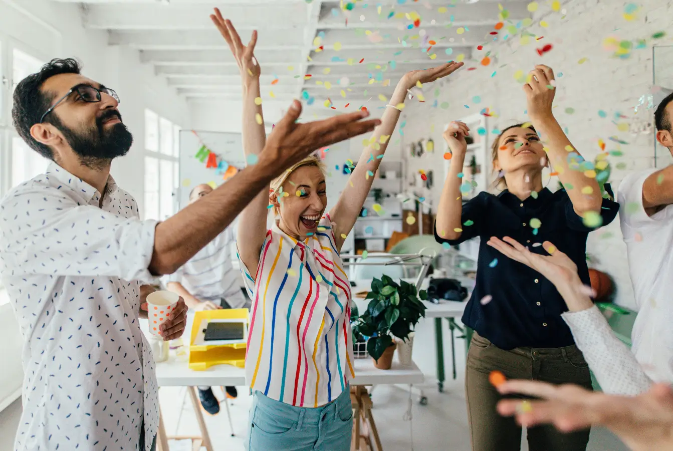 Group of people celebrating with confetti in a bright room.